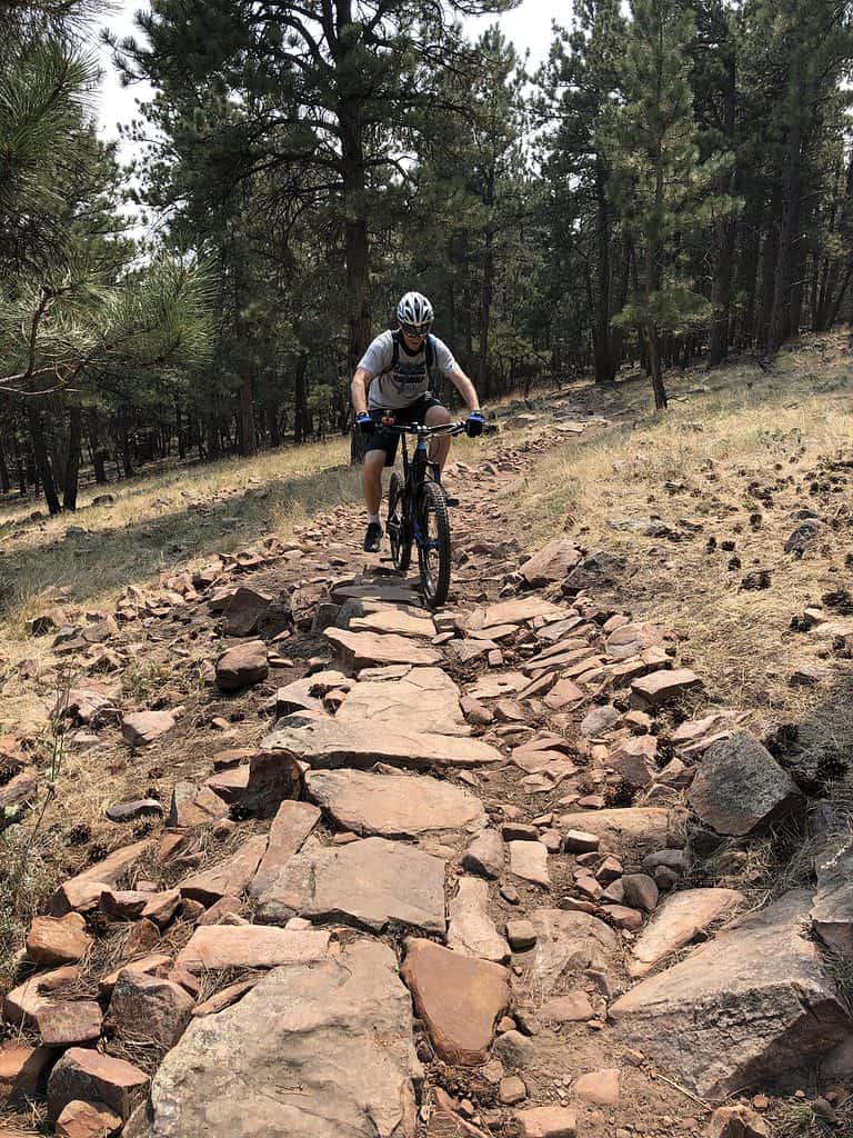 Man mountain biking on a rocky trail through pine forests in Colorado