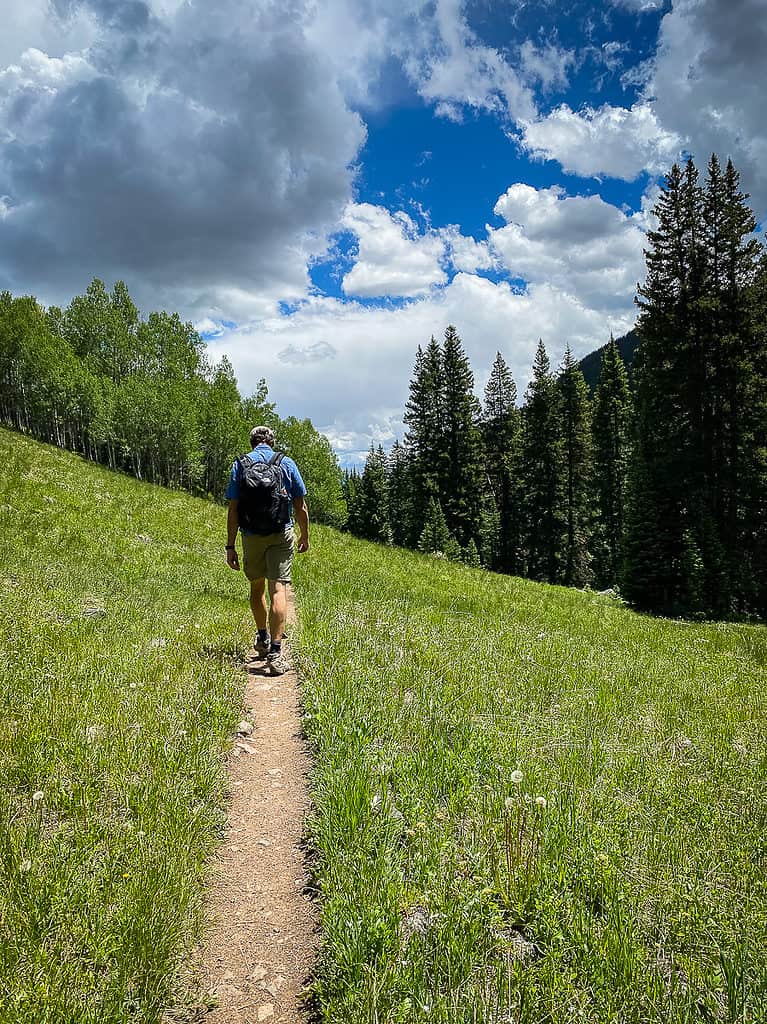 Man hiking a trail through green meadows and pine trees in Breckenridge Colorado. Hiking is one of the best things to do in Breckenridge