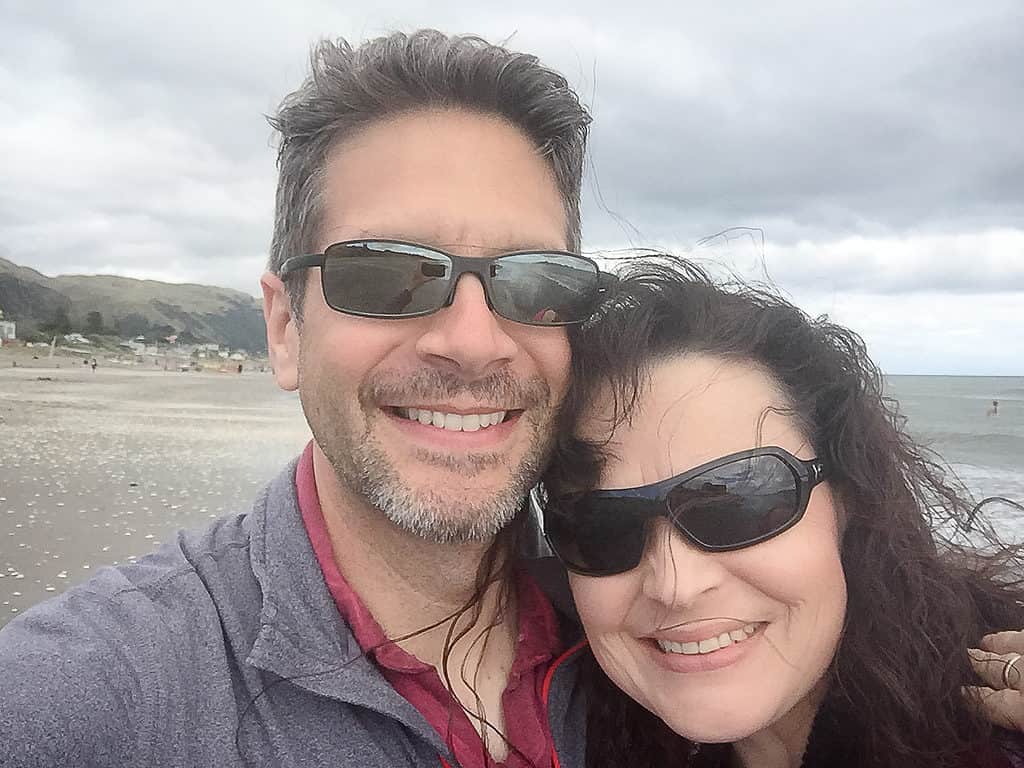 Couple taking a selfie on a windy beach in New Zealand, smiling together on a couples getaway.