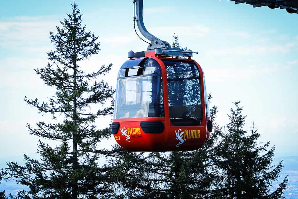 20220905 Anniversary 2237 LRE Web Red Pilatus gondola cabin suspended above pine trees on Mt. Pilatus.