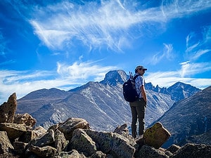 Hiking with the best travel backpack for Europe. Hiker standing on rocky terrain with mountain peaks in the background, showcasing lightweight hiking gear on a high‑elevation trail.