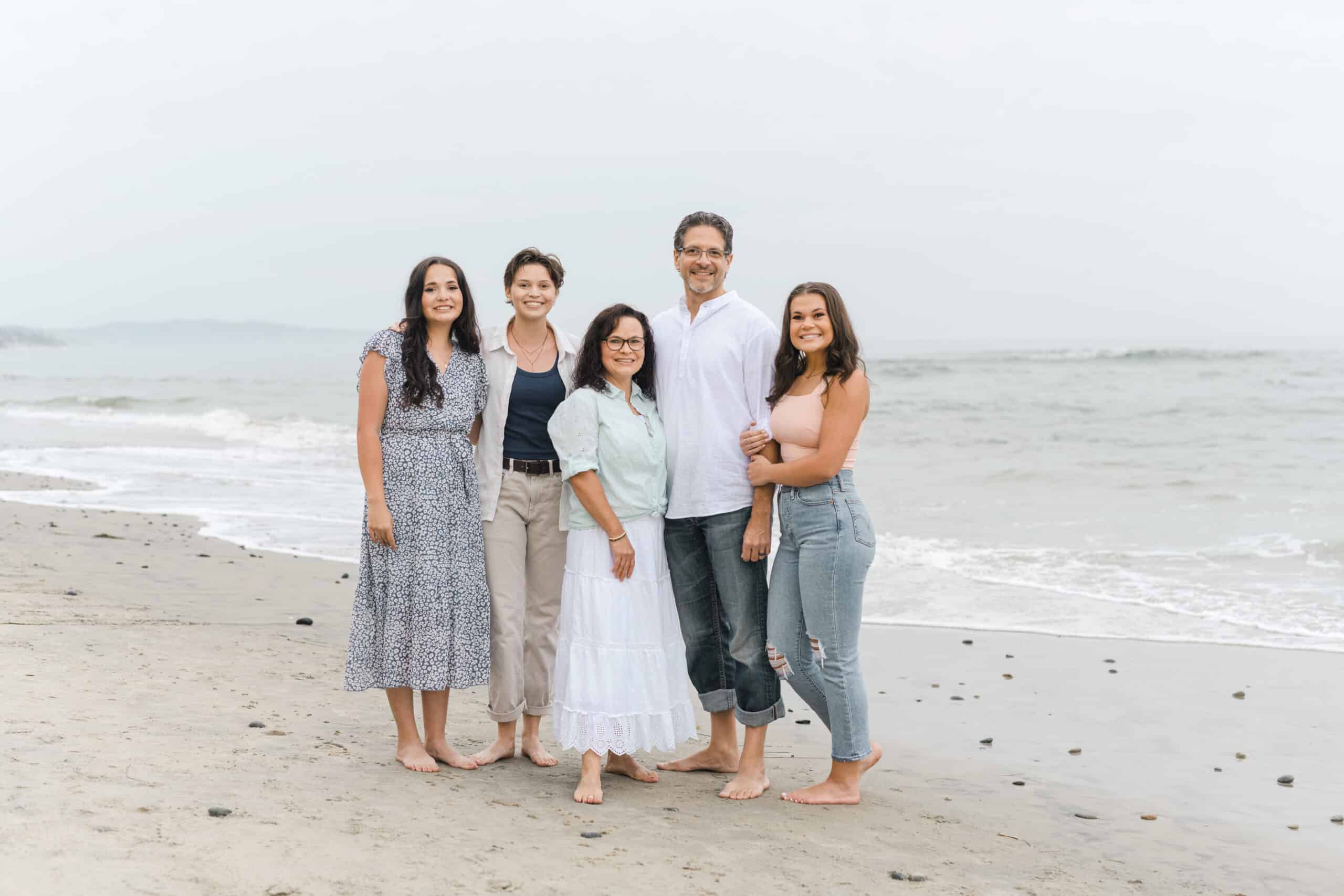 A family standing together on a sandy beach with gentle waves behind them, highlighting family photography on vacation.
