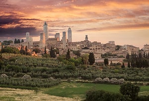 San Gimignano Tuscany Italy skyline at sunset with medieval towers and dramatic orange sky, highlighting planning a trip to Italy.