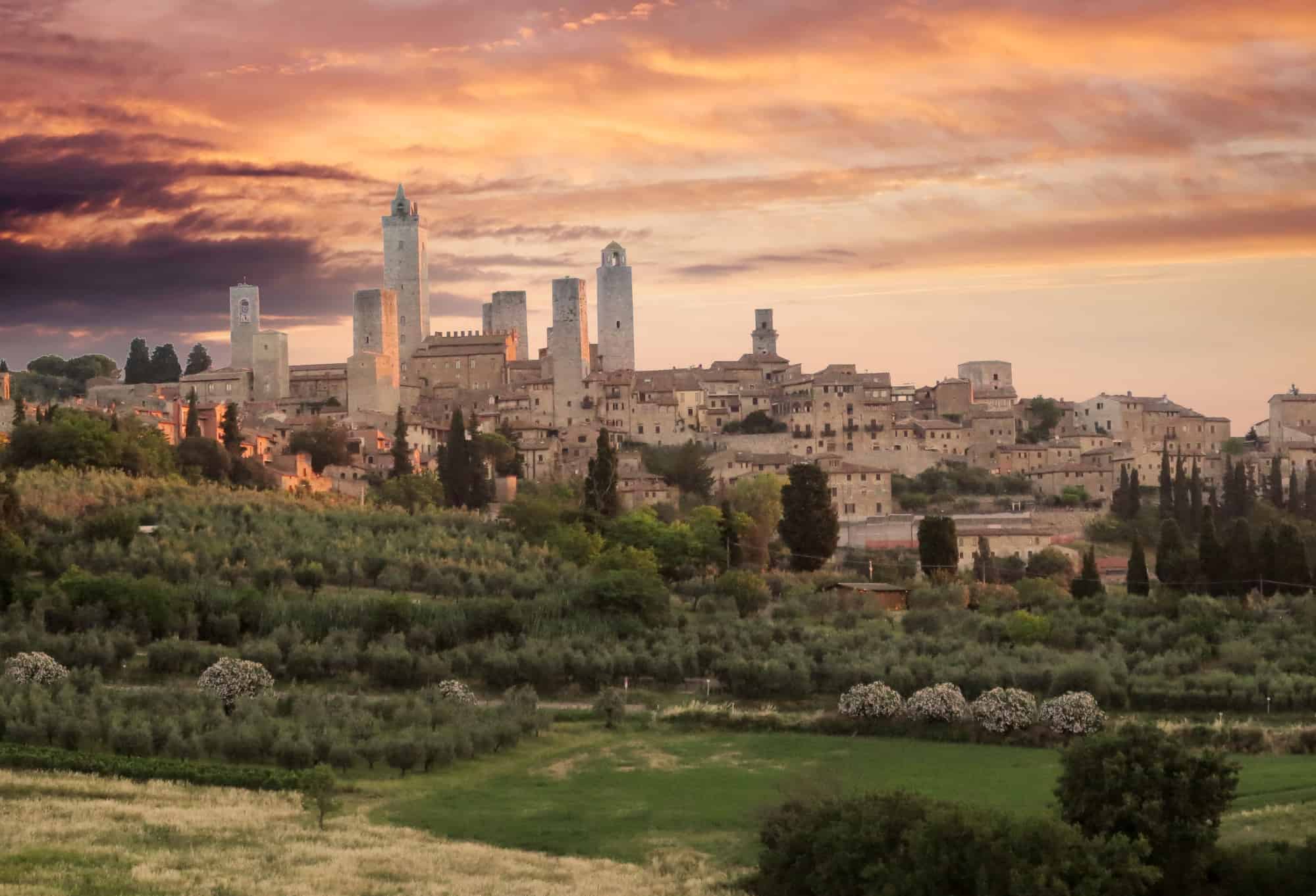 San Gimignano Tuscany Italy skyline at sunset with medieval towers and dramatic orange sky, highlighting planning a trip to Italy.