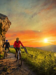 Mountain biking women and man riding on bikes at sunset mountains. Outdoor sport for an epic adventure bucket list.