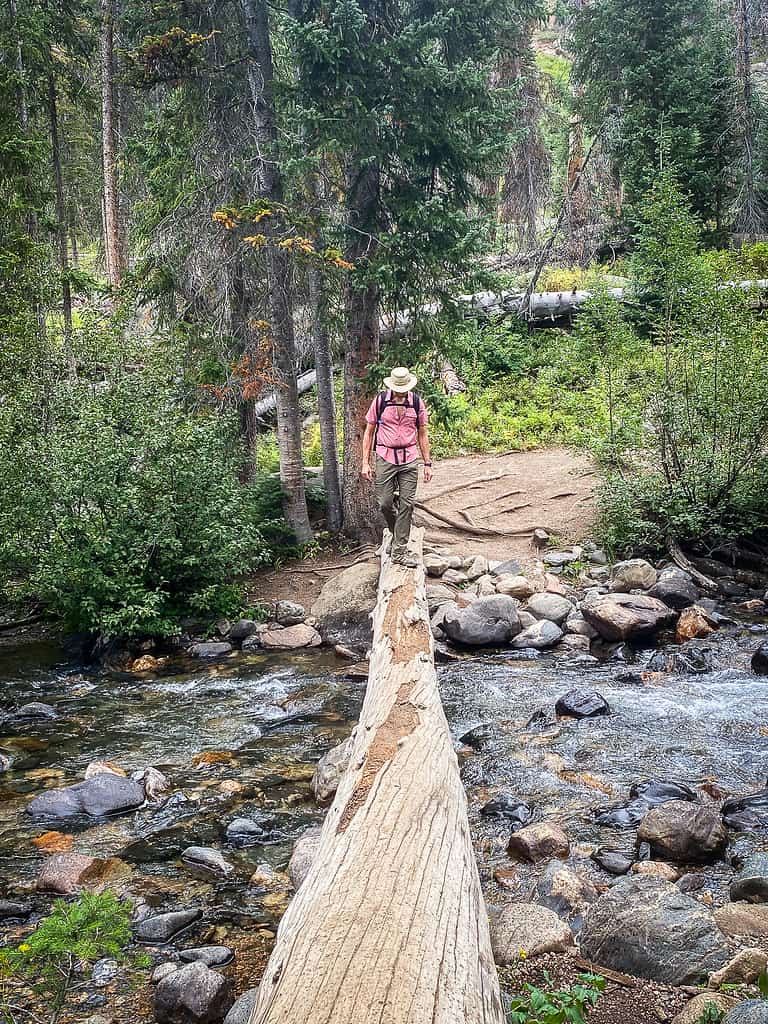 Man hiking to Gold Creek Falls in Steamboat Springs, Colorado and crossing the river on a fallen log.