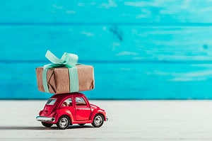 Red car with package tied to the top represents adventures that are great travel gifts.