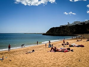 A sunny Algarve beach with people relaxing on the sand near cliffs and whitewashed buildings, highlighting fun things to do in the Algarve.