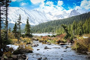 Long Lake framed by snow dusted peaks and pine trees on a Rocky Mountain National Park itinerary. Mountain quotes come alive with snow-capped peaks, evergreen forest, and a rocky stream in Rocky Mountain National Park.