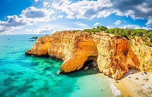 Golden cliffs, turquoise water, and a sandy Algarve beach with umbrellas and sunbathers, highlighting an Algarve beach bucket list.