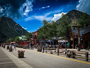 A lively mountain‑town street lined with rustic shops, outdoor cafés, and dramatic peaks in the background, highlighting charming mountain towns in Colorado.