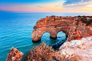 Dramatic coastal rock arches rising above calm blue water at sunset in the Algarve makes for instagrammable spots in the Algarve.