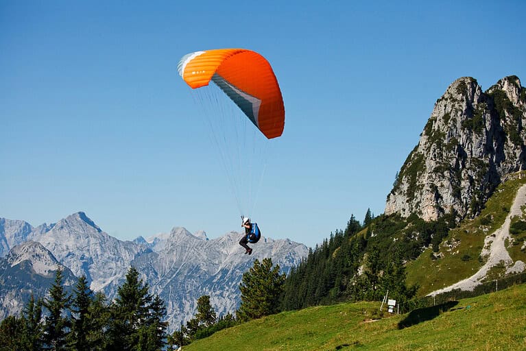 Paragliding by Hogr Paragliding Mt Pilatus with an orange paraglider soaring above the Swiss Alps.