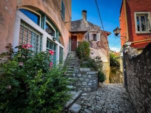 A narrow cobblestone alley with stone steps winding between colorful old buildings in Rovinj, Croatia.