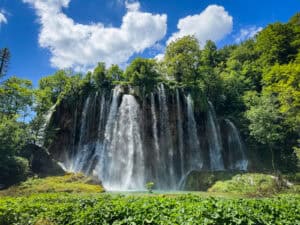 A wide waterfall cascading over rocky cliffs surrounded by green trees, perfect for a guide to exploring plitvice lakes national park.