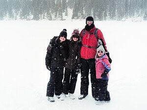 Family bundled up in winter gear, standing in the snow before a winter hiking trip in Colorado.
