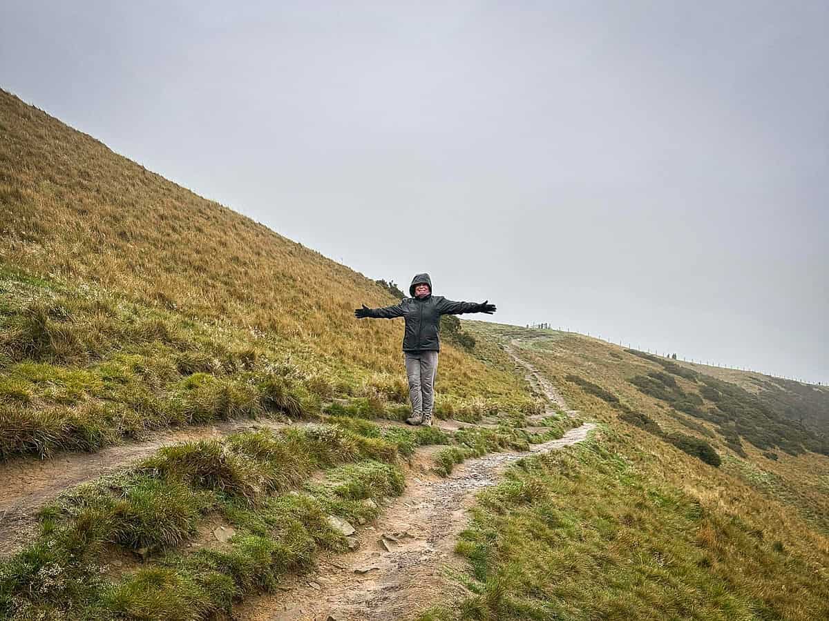 20251116 mamtor 7220 Woman standing on the side of Mam Tor in the cold and rain.