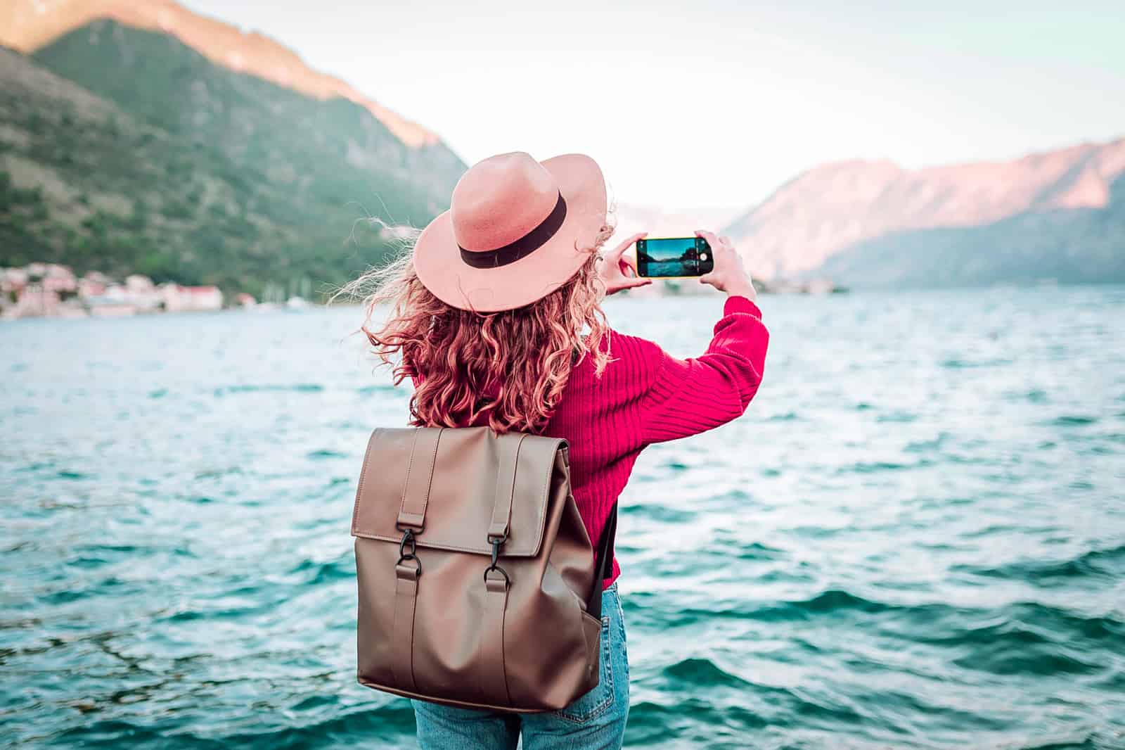 Traveler photographing mountain lake with iPhone on a sunny day using iPhone Travel Photography Tips