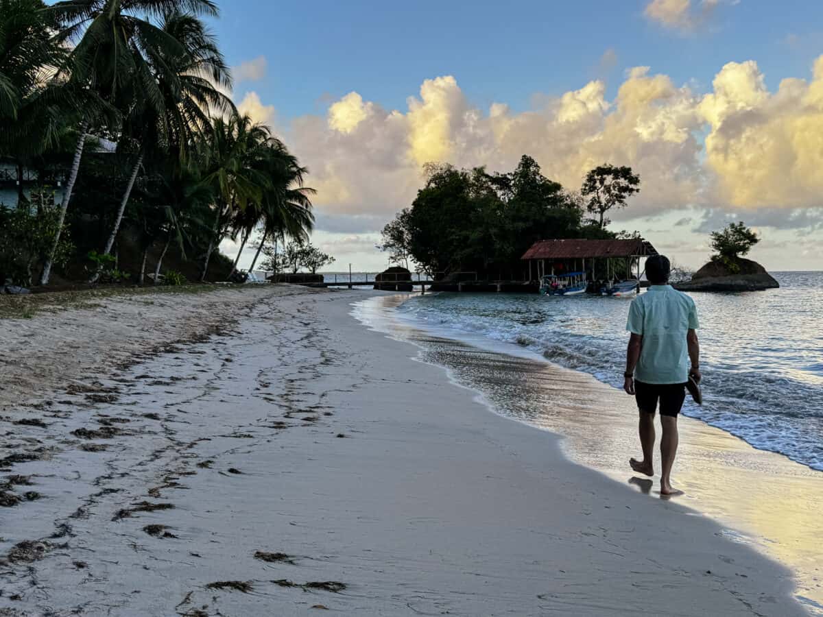 Person walking along a tropical beach at sunset near a small dock and boats in Panama.