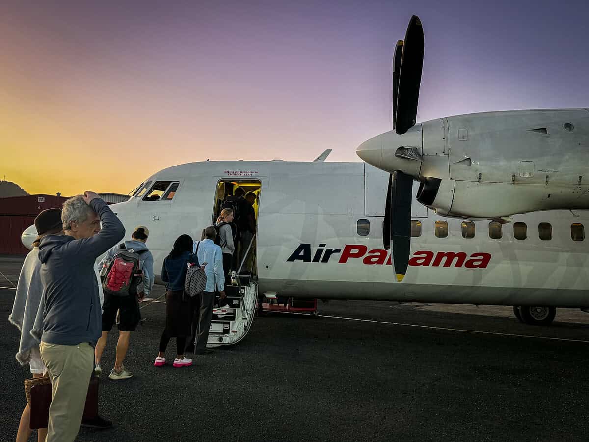Travelers boarding an Air Panama turboprop plane at sunrise, with passengers lined up on the tarmac and the sky glowing in early‑morning colors.