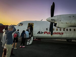 Travelers boarding an Air Panama turboprop plane at sunrise, with passengers lined up on the tarmac and the sky glowing in early‑morning colors.