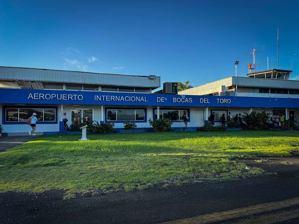 A small blue‑and‑white airport building at the Bocas del Toro International Airport in Panama, with travelers walking outside under clear skies.