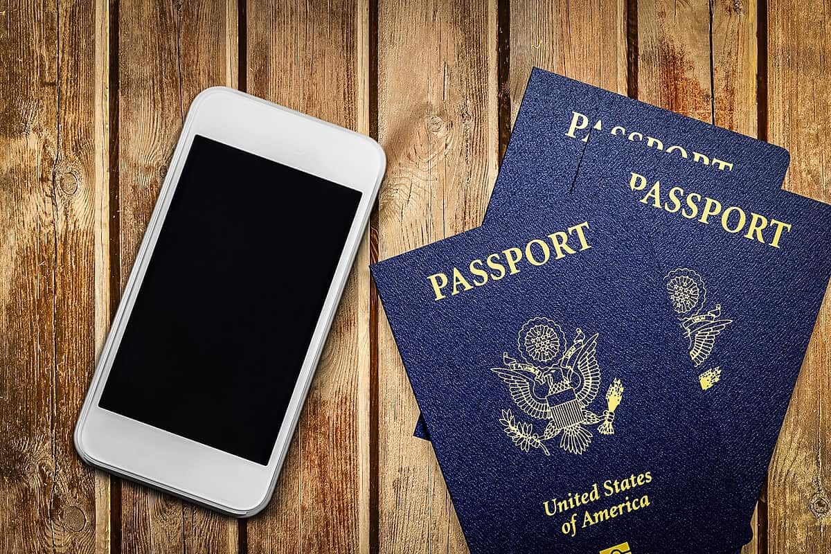 20260211 howtokeeptraveldocumentssafe 1003 A smartphone and three U.S. passports on a wooden surface, representing how to keep travel documents safe while traveling.