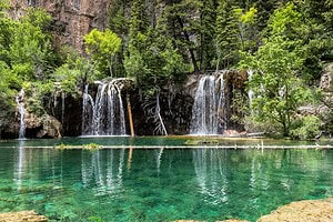 A small waterfall flowing into a clear blue‑green pool surrounded by evergreens and rocky cliffs, highlighting things to do in Glenwood Springs.