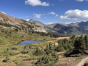 Small alpine lake nestled in a mountain meadow with rocky peaks on tips for visiting Rocky Mountain National Park