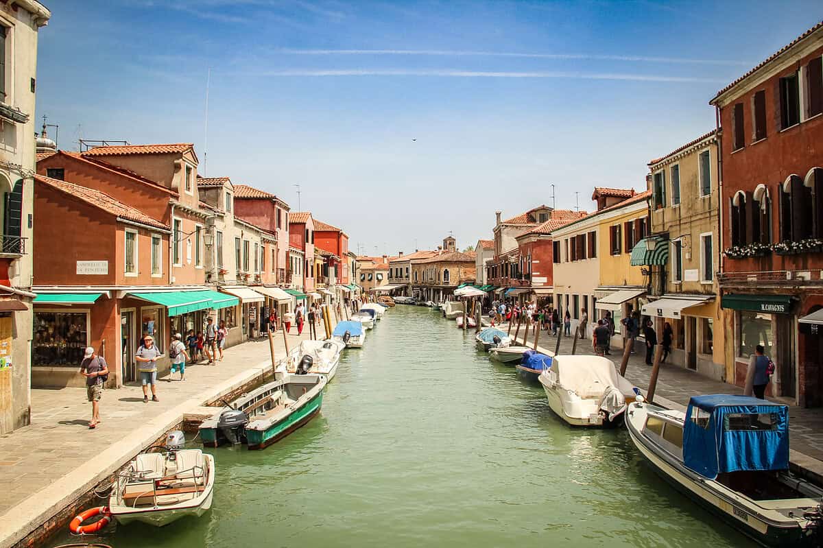 20180530 Murano 7165 Boats lining a sunny canal in Murano Italy with colorful buildings reflected in the water, one of the most beautiful places in Italy for photographers
