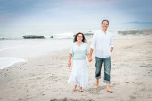 Couple walking hand in hand barefoot on the beach with ocean waves in the background, perfect for a guide to couples getaway ideas.