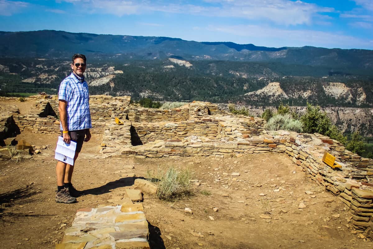 Chris standing among the Great House Pueblo ruins with sweeping San Juan National Forest views at Chimney Rock National Monument.