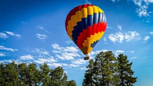 Pagosa Springs hot air balloons rising over the pines with the San Juan Mountains in the background.