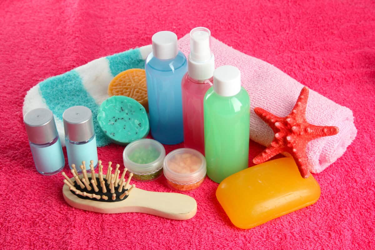 Travel-size shampoo, conditioner, soap bars, and a hairbrush arranged on a pink towel.