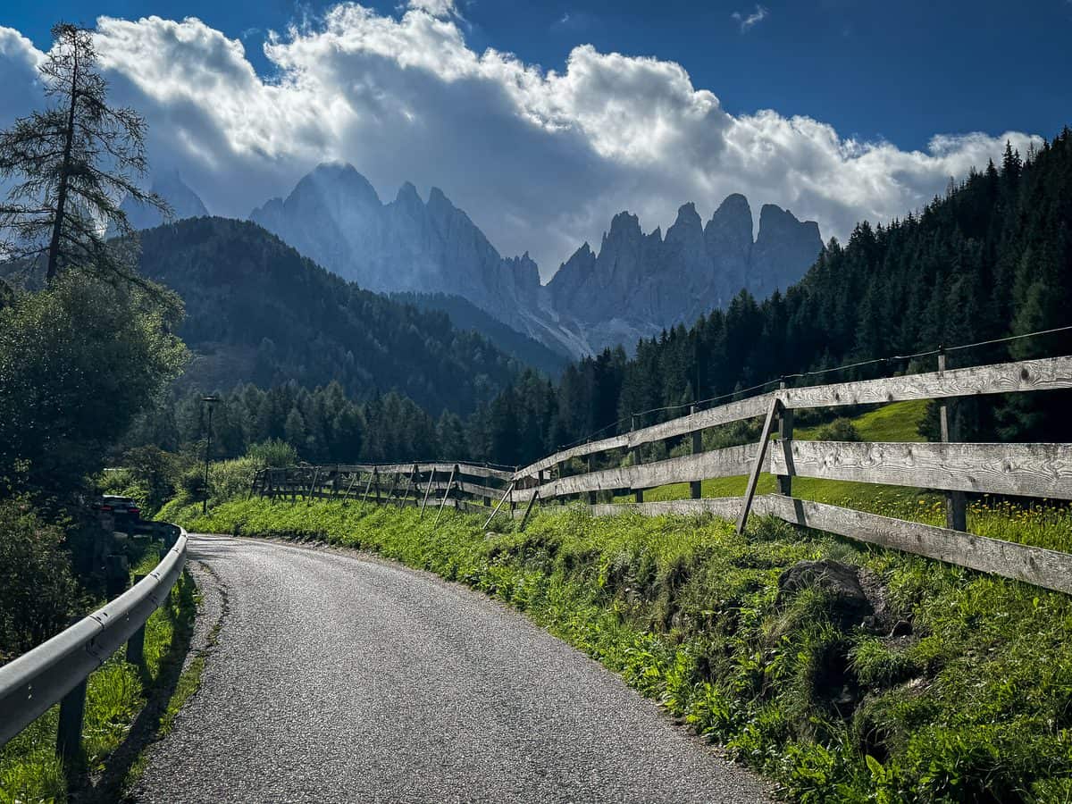 A narrow paved road curves through Val di Funes toward the jagged Odle peaks on our Dolomites road trip.