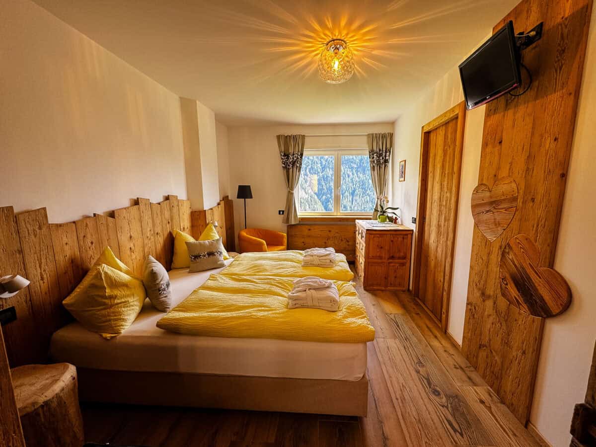 20260824 wheretostayinthedolomites 2455 Wood-paneled bedroom with yellow bedding inside our vacation rental in Colle Santa Lucia, Italy.