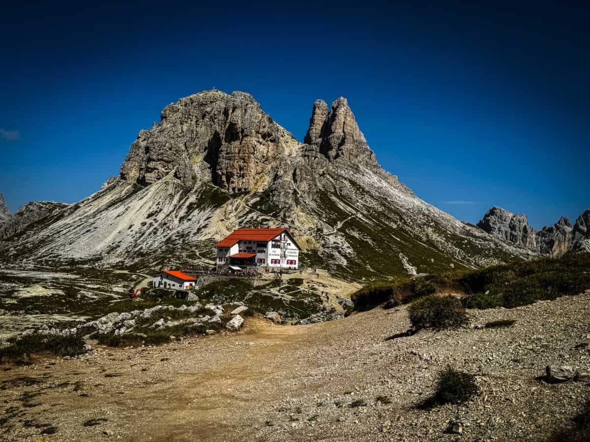 Rifugio Dreizinnenhütte (Rifugio Locatelli) with red roofs below a rocky peak on the Tre Cime di Lavaredo hike in the Dolomites.