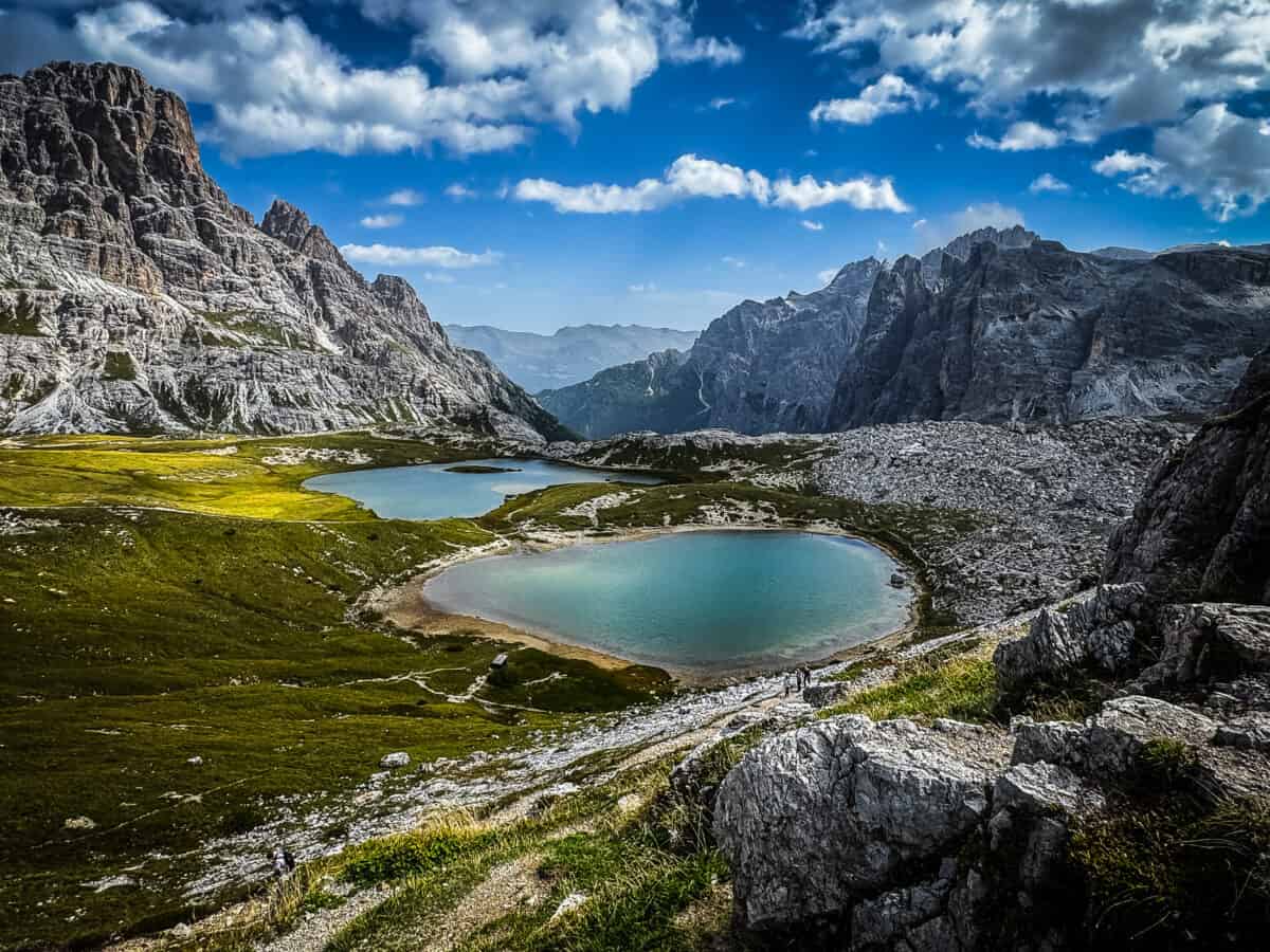 Two turquoise Laghi dei Piani lakes surrounded by green meadows & rocky peaks near Tre Cime di Lavaredo in the Dolomites.