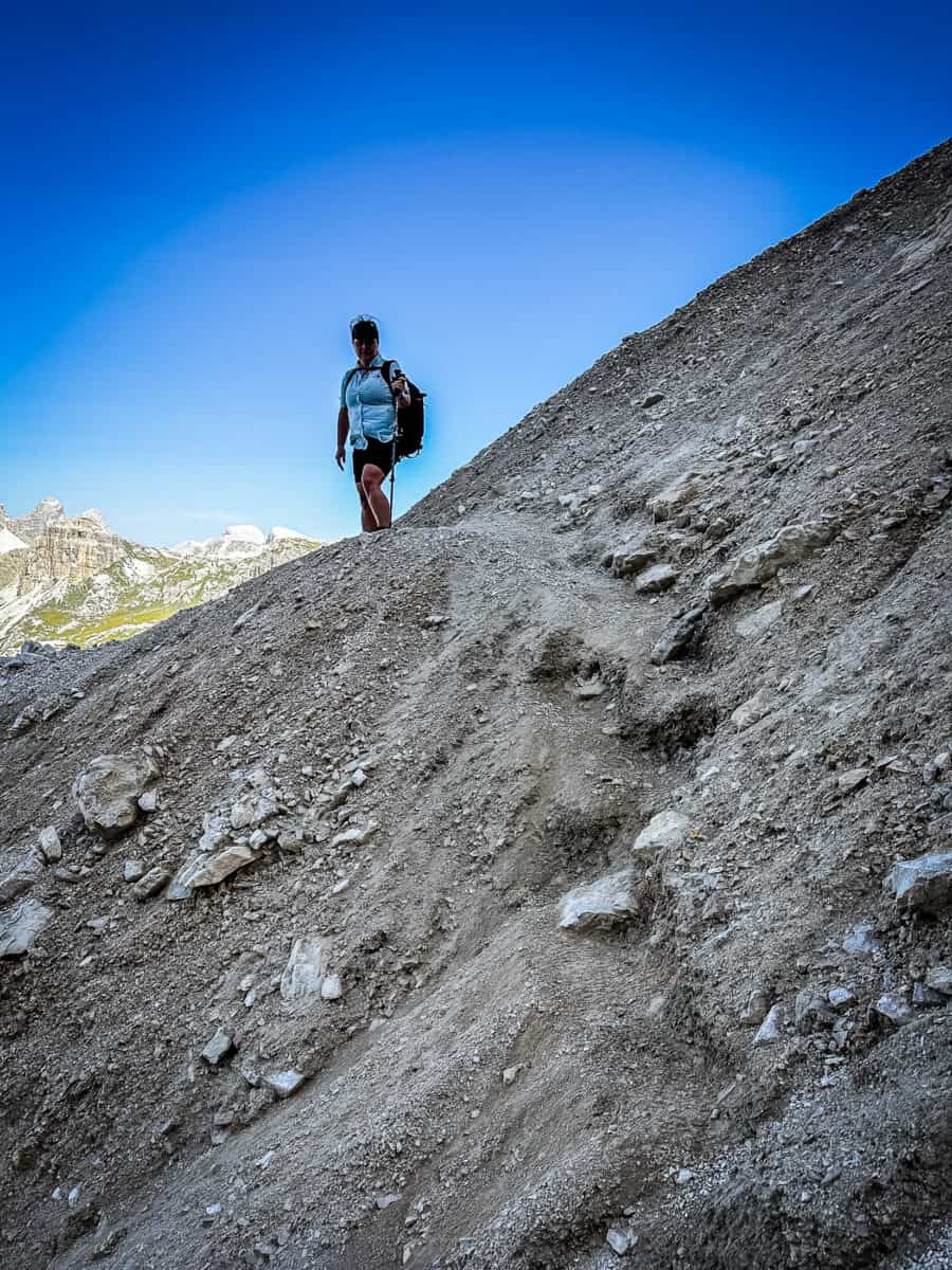 Hiker standing on a steep, loose rockslide where the trail washed out on the upper route of the Tre Cime di Lavaredo hike.