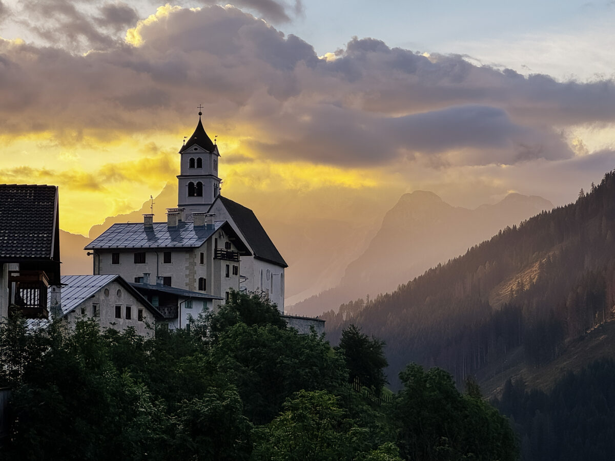 20260829 wheretostayinthedolomitesitaly 3124 Sunrise view of the chapel and village of Colle Santa Lucia from my vacation rental window in the Dolomites, Italy.