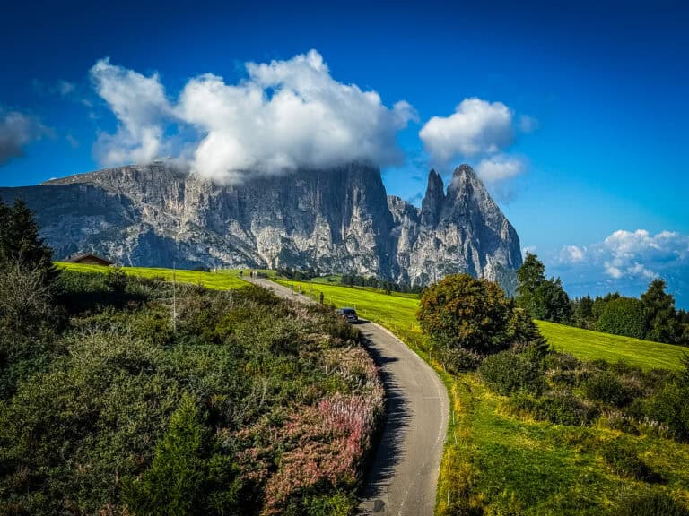Road winding through Alpe di Siusi meadow toward the cloud-capped Schlern, highlighting one of the best things to do in the Dolomites.