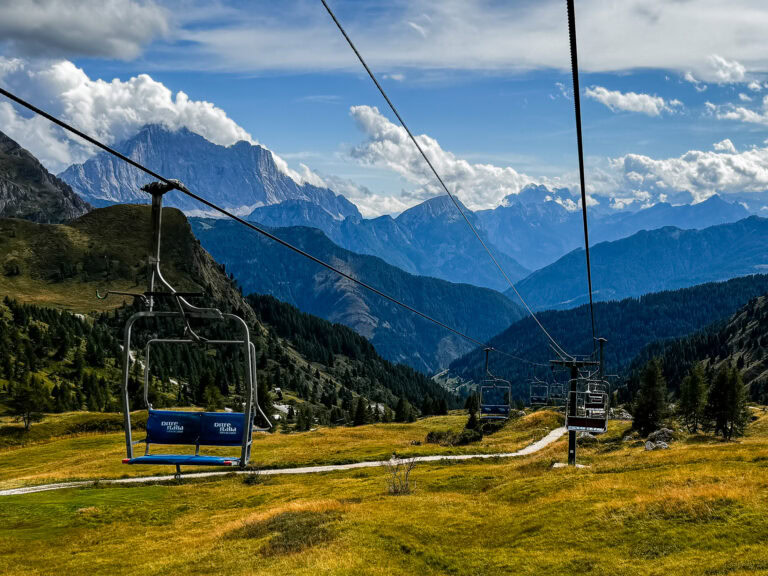 Blue chair on the Fedare chairlift above Passo Giau, one of the Dolomites cable cars, with jagged peaks and clouds behind it.